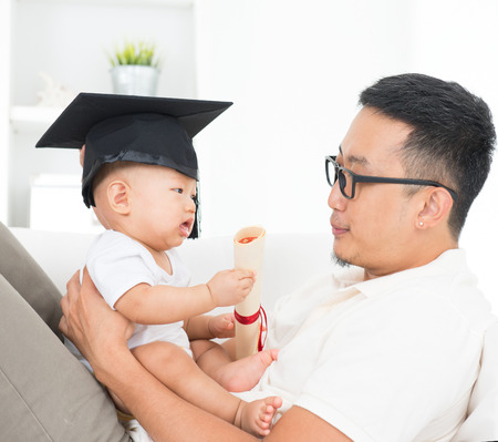 Asian family lifestyle at home. Baby with graduation cap holding certificate. Child and father early education concept.の写真素材