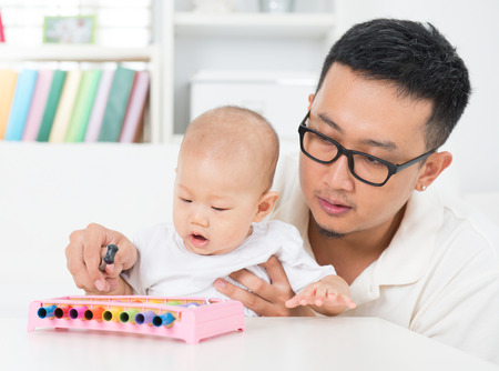 Asian family lifestyle at home. Father playing music instrument with baby. Sound development concept.の写真素材