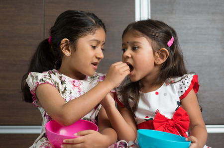 Indian girls sharing food, murukku with each other. Asian sibling or children living lifestyle at home.の写真素材