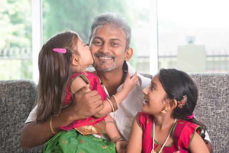 Happy Indian family at home. Asian girl kissing her father, sitting on sofa. Parent and children...