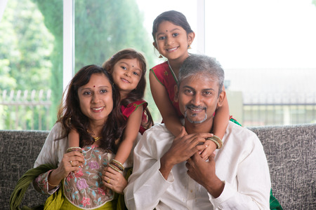 Happy Indian family at home. Asian parents piggyback their kids, sitting on sofa. Parents and...