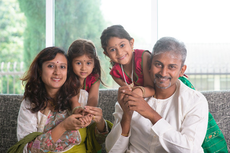 Happy Indian family at home. Asian parents with their kids, sitting on sofa. Parents and children...