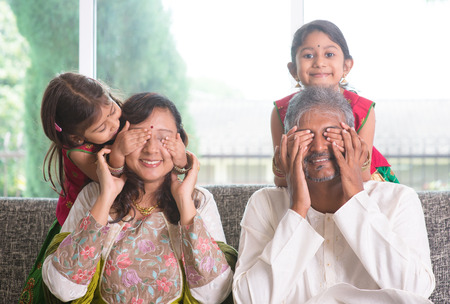 Indian family living lifestyle at home. Cute girls in traditional sari costume covering father and mother eyes. Asian parents and children.の写真素材