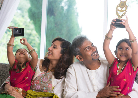 Happy Asian Indian family at home. Kid raised their trophy high up, education achievement concept. Parents and children indoor lifestyle.の写真素材