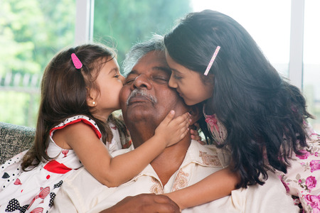 Portrait Indian family at home. Grandchildren kissing on grandparent face. Asian people living lifestyle.の写真素材
