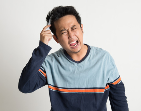 Asian man combing his tangled hair in a morning after woke up, on plain background.の写真素材