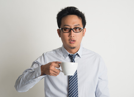 Tired Asian businessman with dark eyes circle holding coffee cup on plain backgroundの写真素材