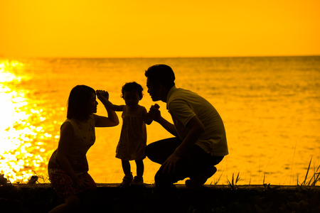 Silhouette of happy Asian family playing at outdoor beach during summer sunset.