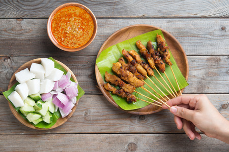 Overhead view people holding chicken satay on wooden dining table, one of famous local dishes.の写真素材
