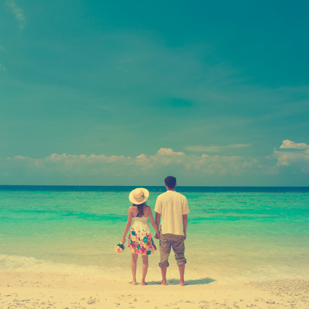 Rear view of couple holding hands walking at beach, in vintage style filter.の写真素材