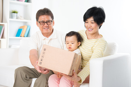 Asian family received an express courier parcel and open it at home, grandparents and grandchild living lifestyle indoor.の写真素材