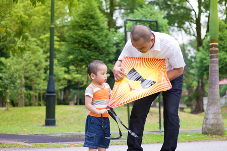 Father teaching son to fly a kite at outdoor garden park. Happy Southeast Asian family living lifestyle.の写真素材