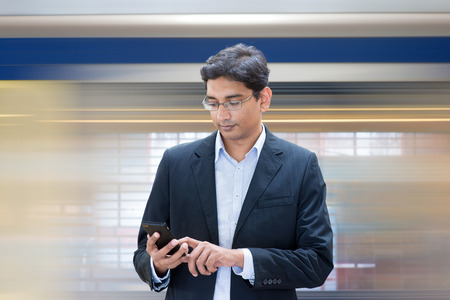 Asian Indian businessman texting using smartphone while waiting train at railway station.の写真素材