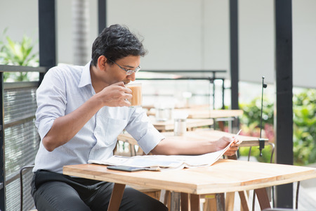 Asian Indian business man reading newspaper while drinking a cup hot milk tea during lunch hour at cafeteria.の写真素材