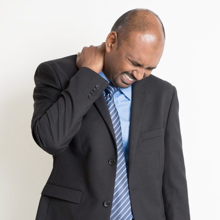 Indian businessman shoulder pain, holding his neck with painful face expression, standing on plain...