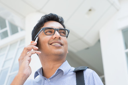 Indian businessman talking on phone in front modern office building.の写真素材