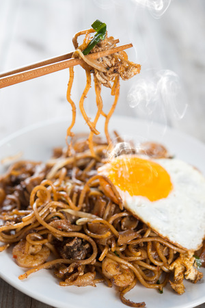 Stir fried char kway teow with prawns and chopstick over wooden background.の写真素材