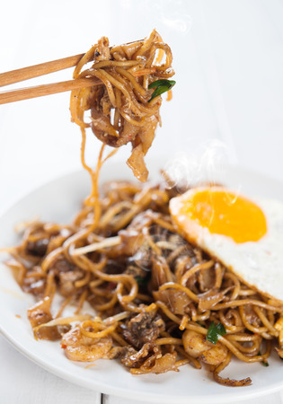 Close-up stir fried char kuey teow on chopstick over wooden background.の写真素材