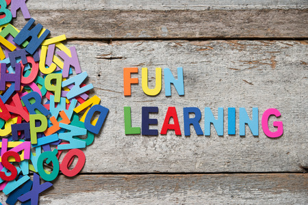 The colorful words "FUN LEANRING" made with wooden letters next to a pile of other letters over old wooden board.の写真素材
