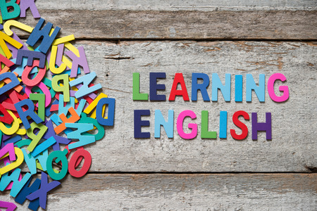 The colorful words "LEANRING ENGLISH" made with wooden letters next to a pile of other letters over old wooden board. The colorful words "LEANRING ENGLISH" made with wooden letters next to a pile of other letters over old wooden board.