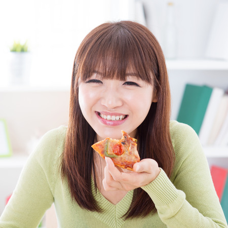Asian female eating pizza at home. Woman living lifestyle indoors.の写真素材