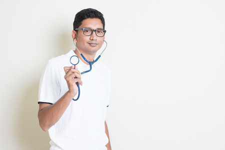 Indian medical student with stethoscope in hand. Asian man standing on plain background with shadow and copy space. Handsome male model.の写真素材