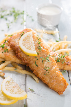 Fish and chips. Fried fish fillet with french fries on bright wooden background. Fresh cooked with hot steams smoke.の写真素材