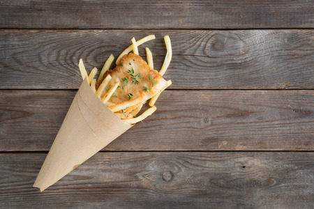 Fish and chips. Overhead view fried fish fillet with french fries wrapped by paper cone, on wooden background.の写真素材