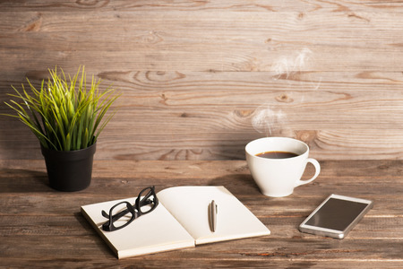 Working table with notepad, coffee cup , pen , smartphone , glasses, plant pot. Wooden table background with copy space on top. Instant photo vintage split toning color effect.の写真素材