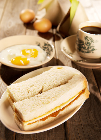 Traditional Malaysian style breakfast, kaya butter toast, nasi lemak and boiled eggs with coffee. Fractal on the cup is generic print. Soft focus setting with dramatic ambient light on dark wooden background.の写真素材