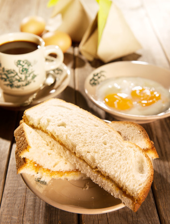 Traditional Chinese Malaysian style breakfast, kaya butter toast, nasi lemak and boiled eggs with coffee. Fractal on the cup is generic print. Soft focus setting with dramatic ambient light on dark wooden background.の写真素材