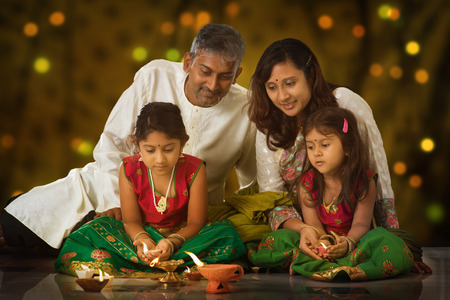 Indian family in traditional sari lighting oil lamp and celebrating Diwali, fesitval of lights inside a temple. Little girl hands holding oil lamp indoors.の写真素材