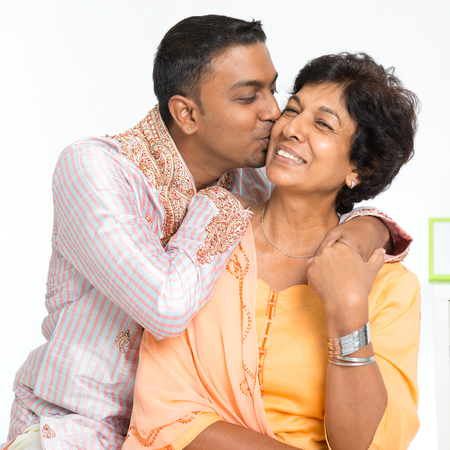 Portrait of happy Indian family at home. Indian 30s grown son kissing his mature 50s mother.の写真素材