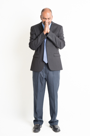 Full length Indian businessman in praying gesture, standing on plain background.の写真素材