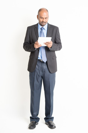Full body Asian Indian businessman using digital tablet computer standing over plain backgroundの写真素材