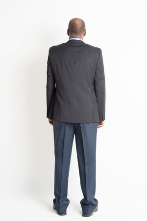 Rear view full body mature Indian business man standing on plain background.の写真素材