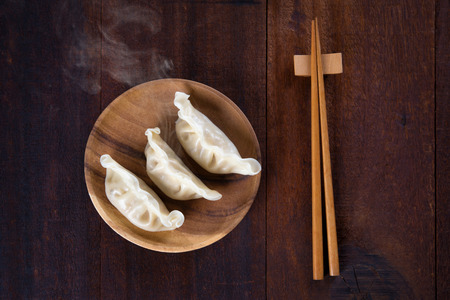Top view fresh dumplings with hot steams on wood plate with chopsticks. Chinese meal on rustic old vintage wooden background.の写真素材
