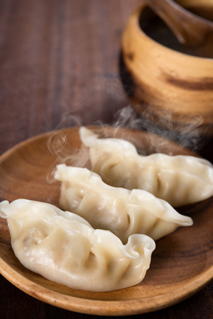 Close up dumplings with hot steams on wood plate. Chinese food on rustic old vintage wooden background.の写真素材