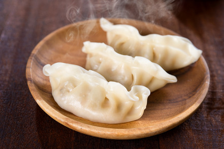 Close up fresh dumplings with hot steams on wood plate. Chinese food on rustic old vintage wooden background.の写真素材