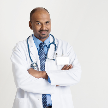 Portrait of mature Indian male medical doctor in uniform standing on plain background with shadow.の写真素材