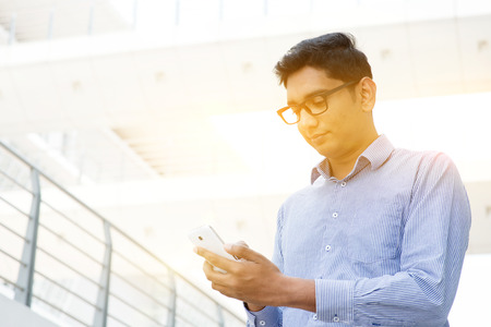 Asian Indian businessman using smartphone, modern urban city sunrise background.の写真素材
