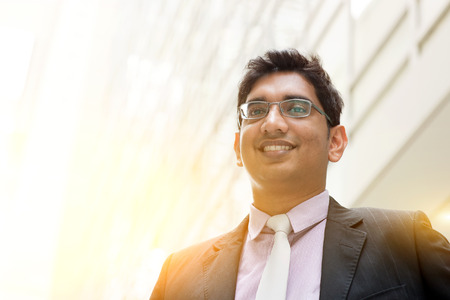 Portrait of handsome Asian Indian business man smiling, outside modern office building block, beautiful golden sunlight at background.の写真素材