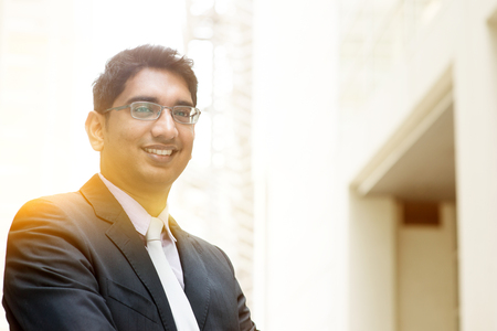 Portrait of Asian Indian business man smiling, outside modern office building block, beautiful golden sunlight at background.の素材 [FY31047875293]