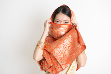 Portrait of secrecy mixed race Indian Chinese woman in traditional sari dress, covering face and looking at camera, on plain background.の写真素材