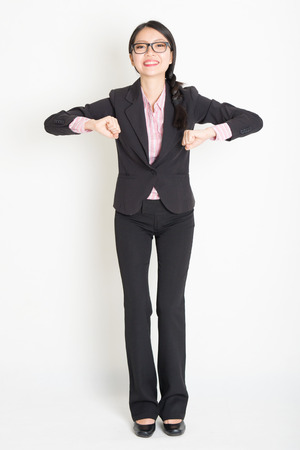 Full length front view of young Asian businesswoman in formalwear ready to jump, standing on plain background.の写真素材