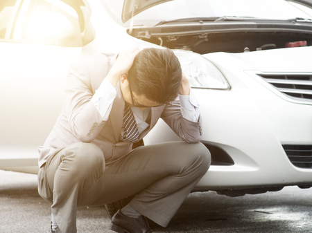 Worried Asian business man squatting beside his breakdown car, feel helpless.の写真素材