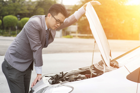 Young Asian business man looking under the hood of breakdown car.の写真素材