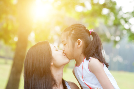 Lifestyle portrait mom and daughter kissing in happiness at the outside in the park. Family outdoor fun, morning with sun flare.の写真素材