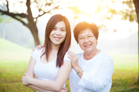 Portrait of beautiful Asian elderly mother and daughter, senior adult woman and grown child. Outdoors family at nature park with beautiful sun flare.の写真素材