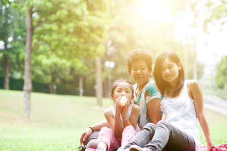 Portrait of multi generation Asian family at nature park. Grandmother, mother and daughter outdoor fun. Morning sun flare background.の写真素材